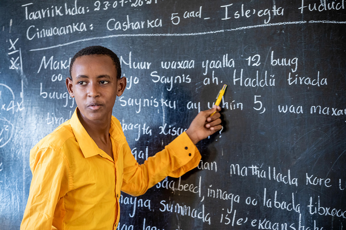 A boy points to handwritten text on a blackboard. 