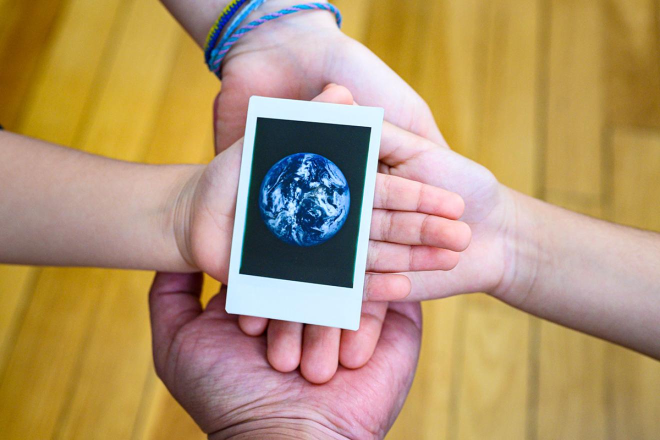 Four hands hold an image of the earth.